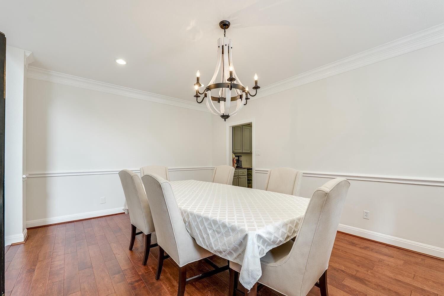Formal dining room with iron-and-wood chandelier, wainscot trim, and hardwood floors