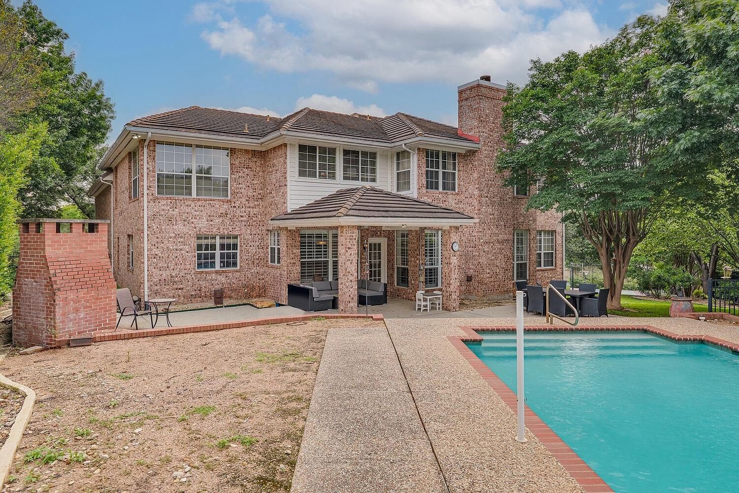 Rear elevation of 14 Torrington Ln, a two-story brick estate with a covered patio and sparkling pool on a rare double lot in The Hills, Texas